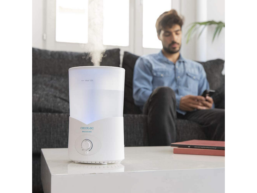 Humidificador blanco con vapor sobre mesa, hombre sentado al fondo.