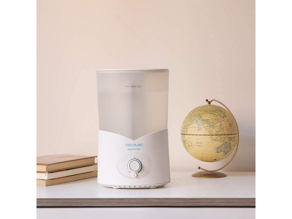 Un humidificador blanco está sobre una mesa junto a libros y un globo terráqueo.