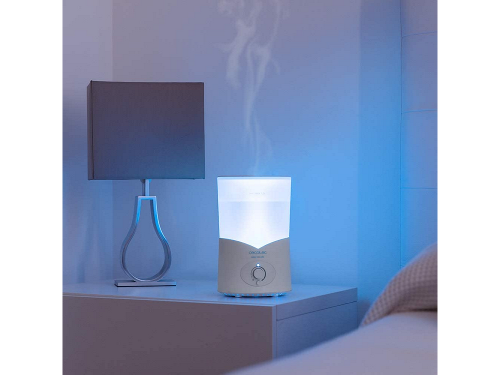 Un humidificador emite vapor junto a una lámpara en una mesita de noche.