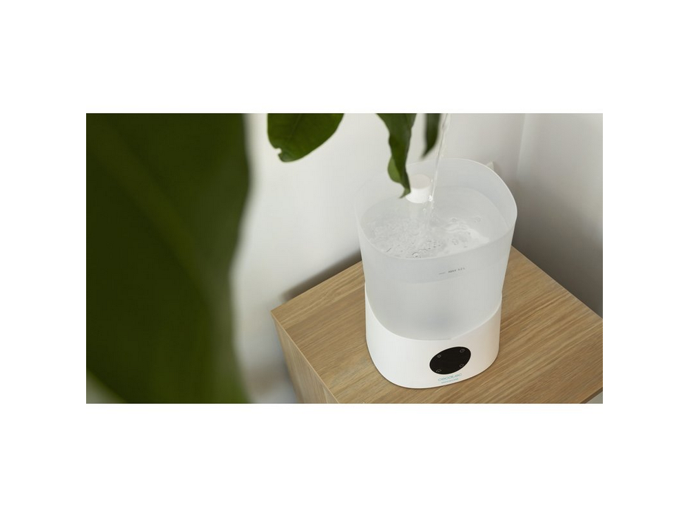 Humidificador sobre mesa de madera. El agua se vierte en el tanque blanco. Hojas verdes en el fondo.