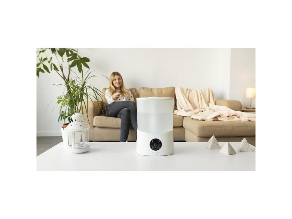 Mujer sentada en un sofá con humidificador en la mesa, plantas al fondo.