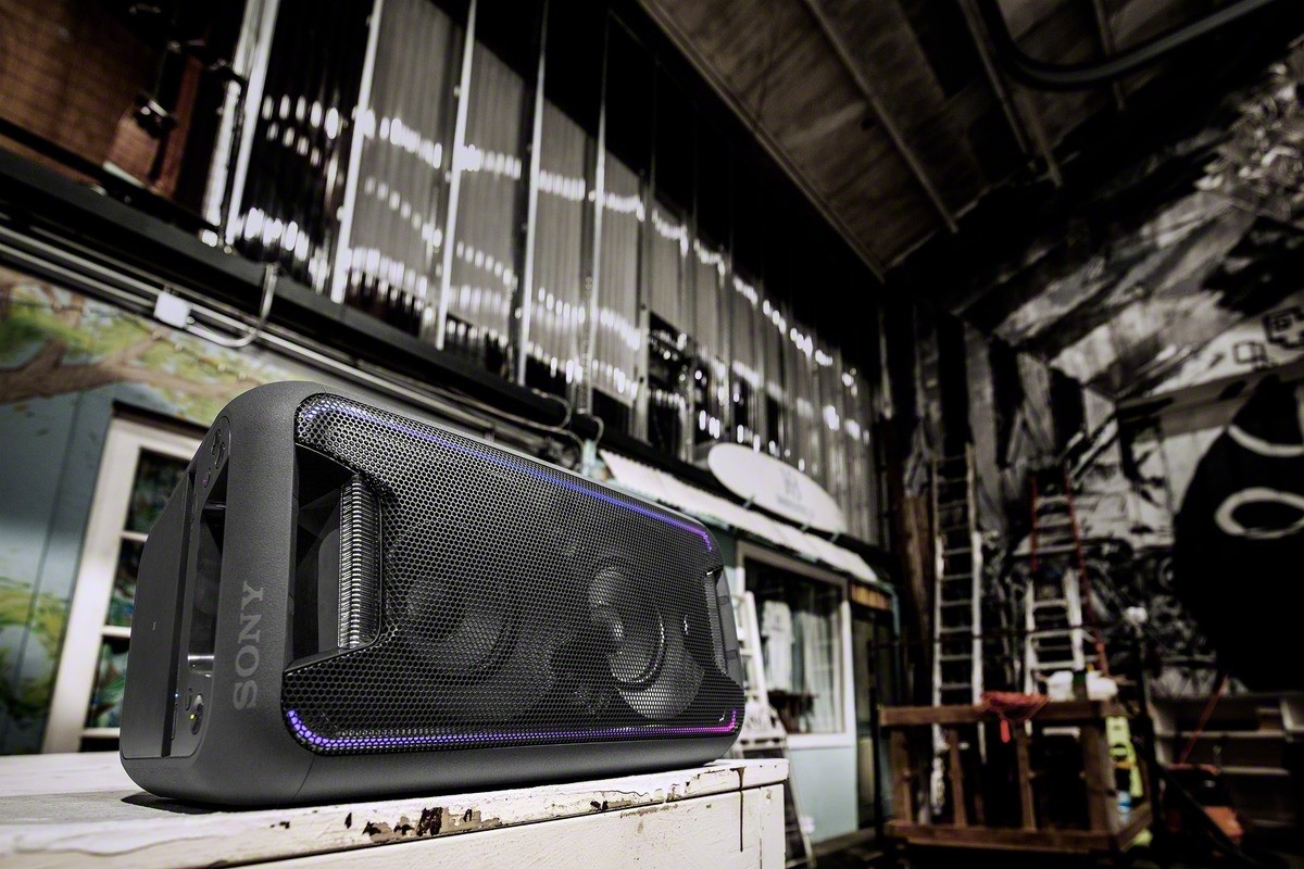 Un sistema de altavoces negro con un panel frontal de malla, colocado en una sala industrial.