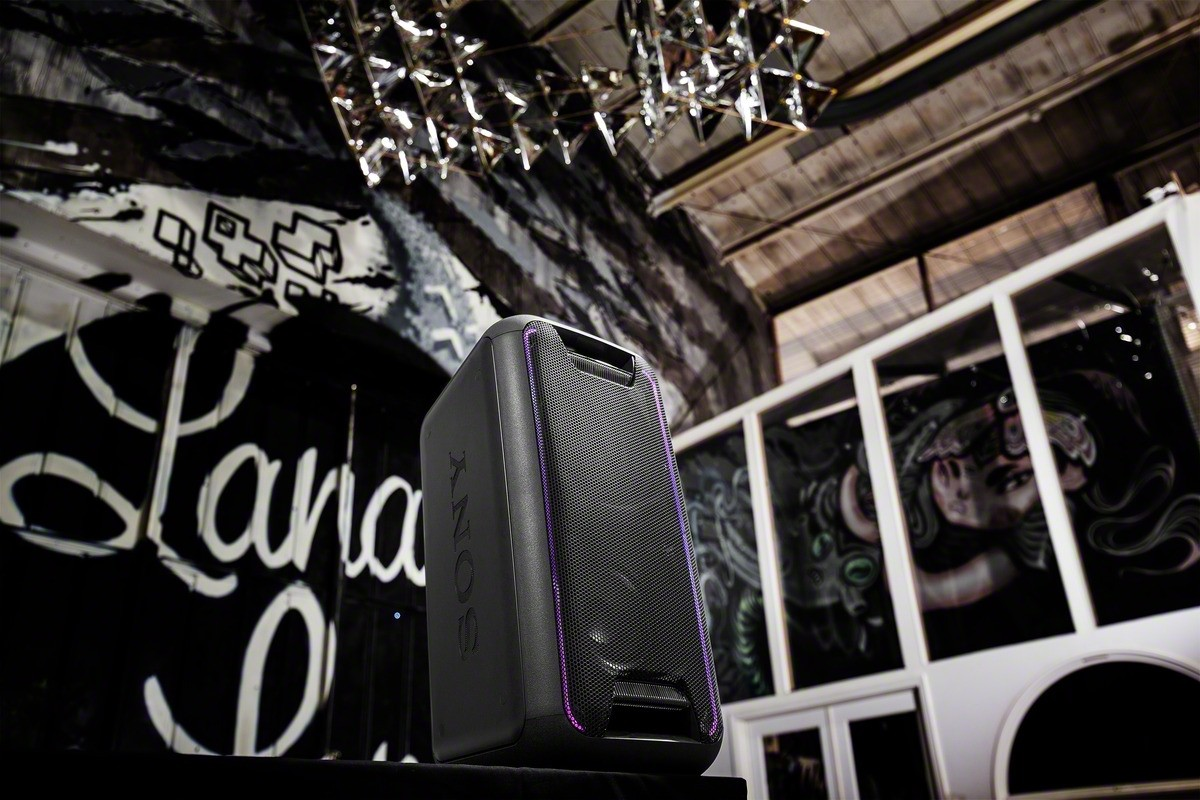 Altavoz Sony sobre un soporte. El fondo presenta arte de graffiti y una lámpara de araña. Luces moradas.