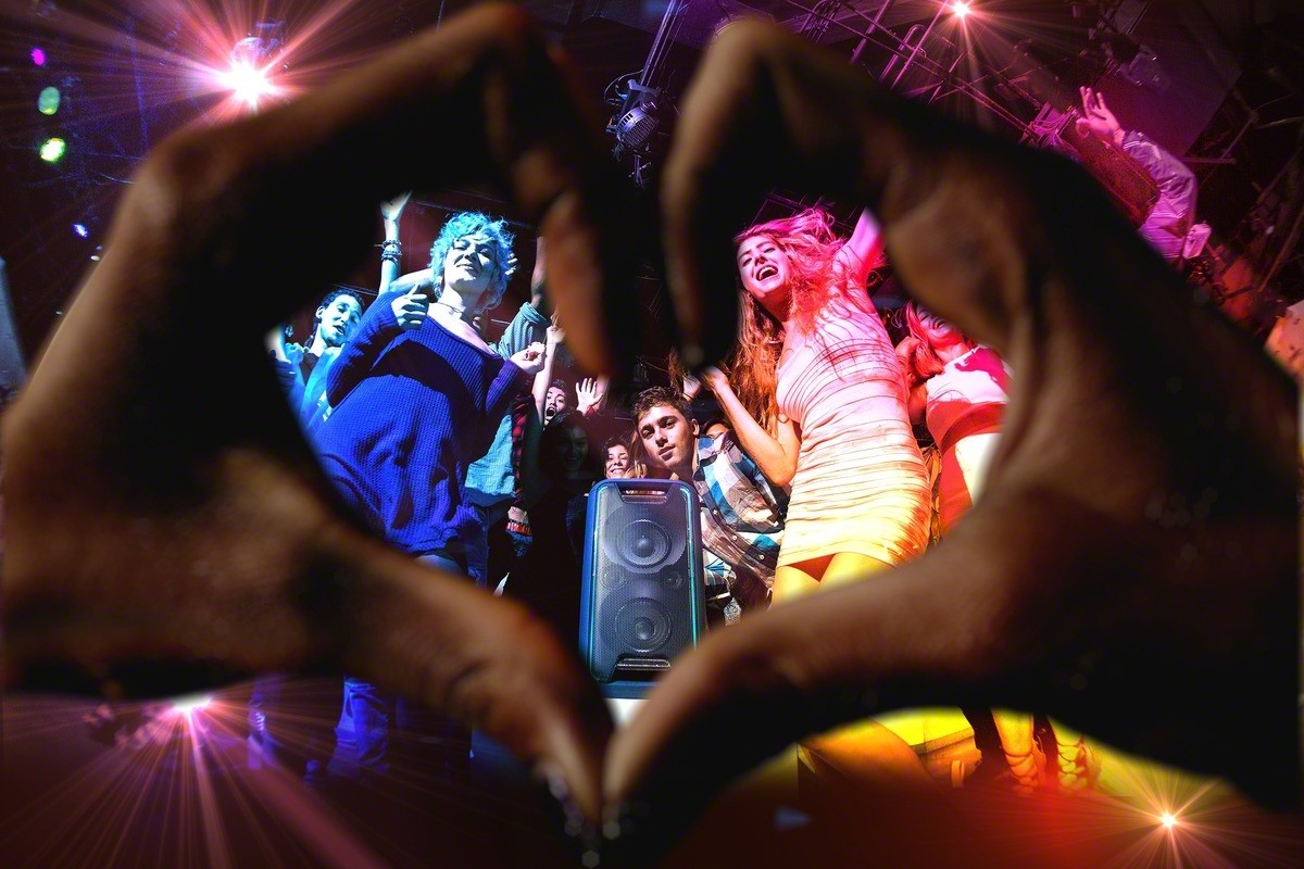 Manos formando un corazón alrededor de una multitud en una fiesta, luces.