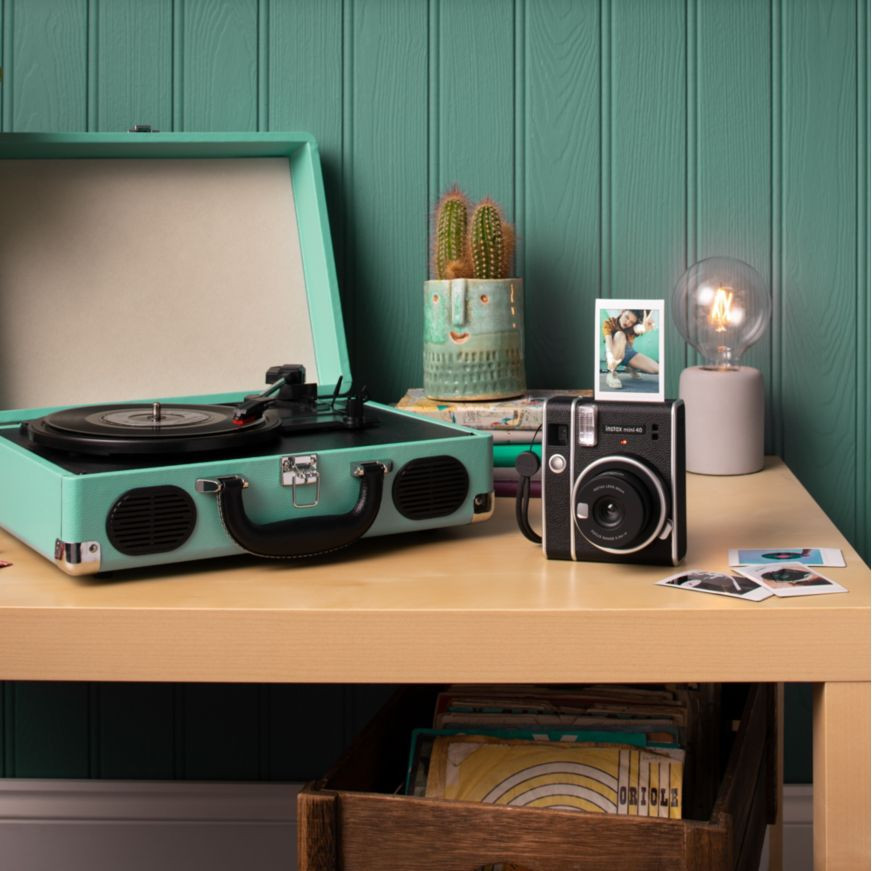 Retro platenspeler, cactus in pot, instantcamera, gloeilamp en foto's op een houten tafel.