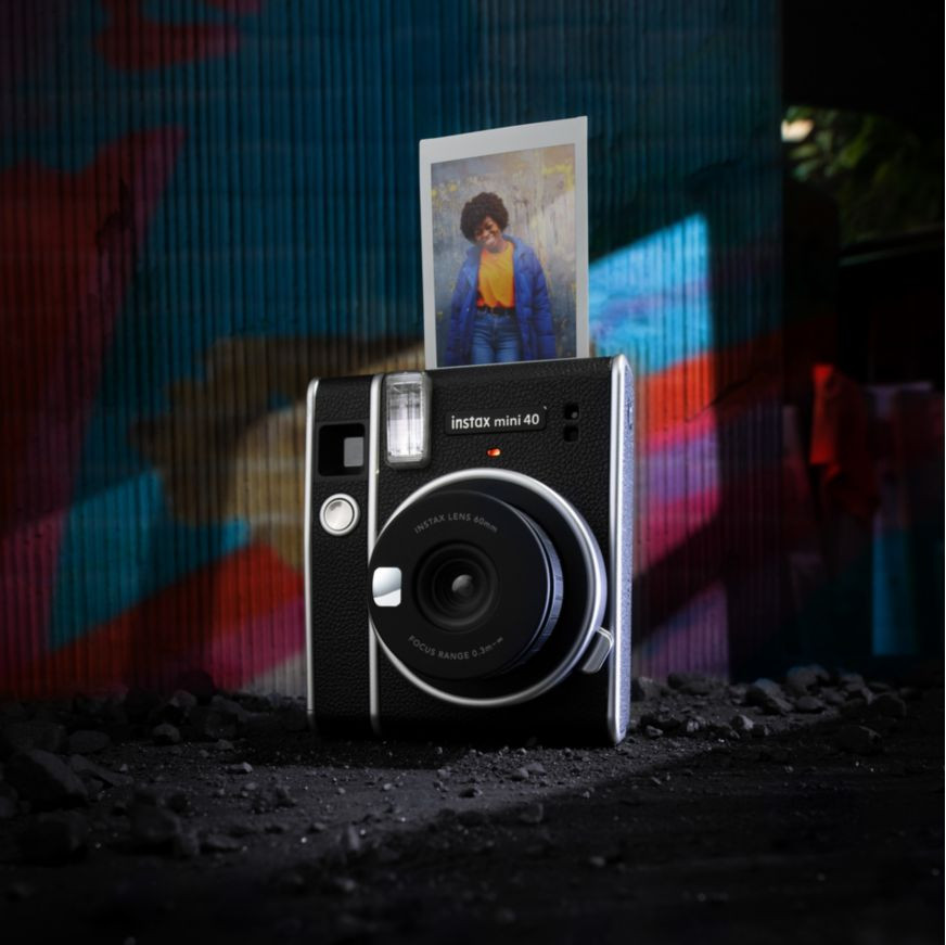Zwarte Instax camera met een foto-afdruk, tegen een graffiti-muur.