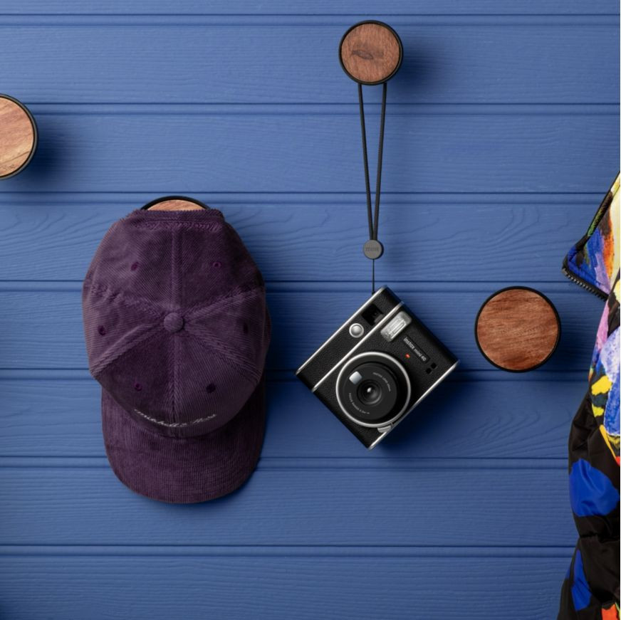 Een paarse pet en een zwarte camera hangen aan een blauwe muur met houten cirkels.