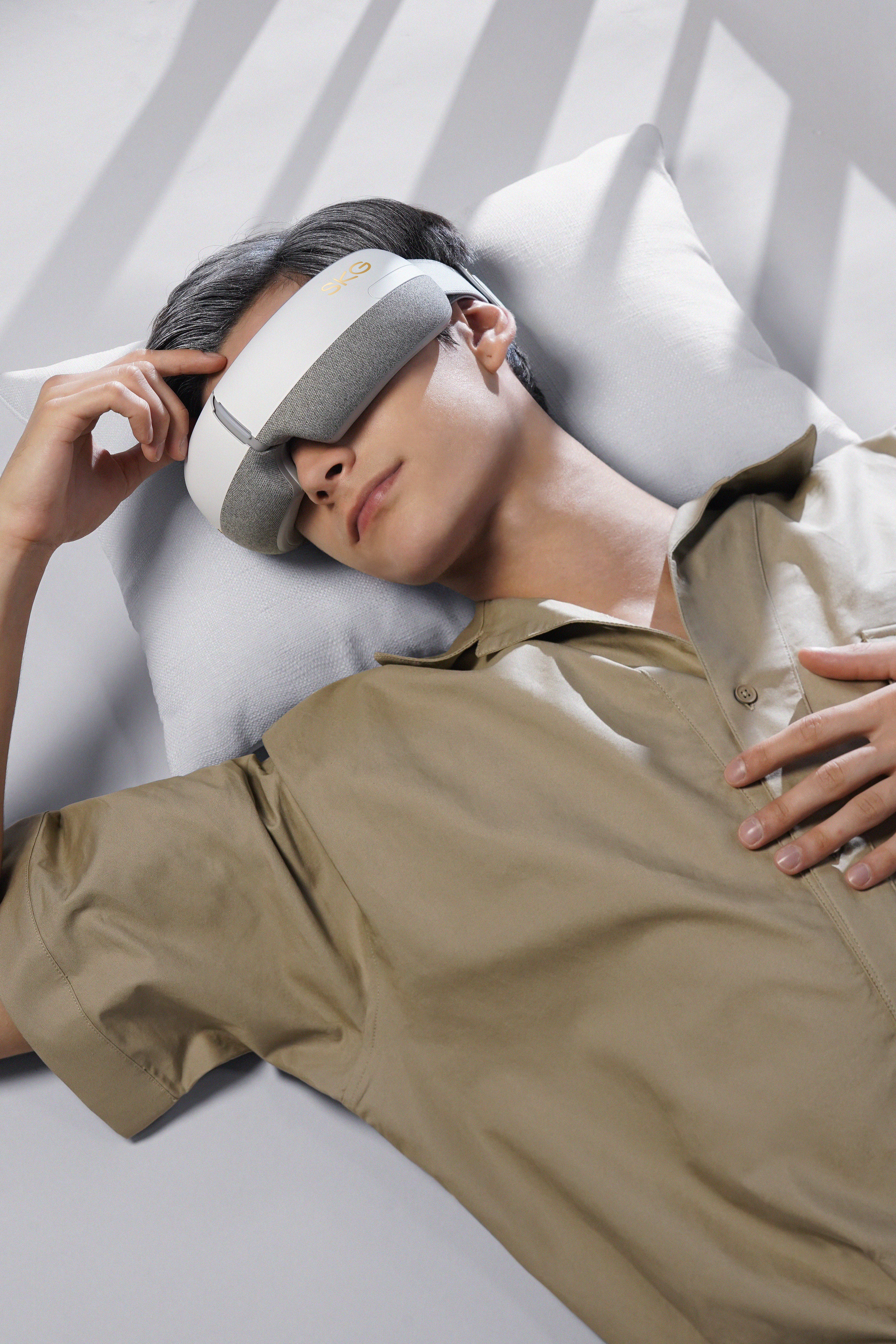 Ein Mann, der einen Augenmassager trägt und auf einem Kissen liegt, Augen geschlossen.
