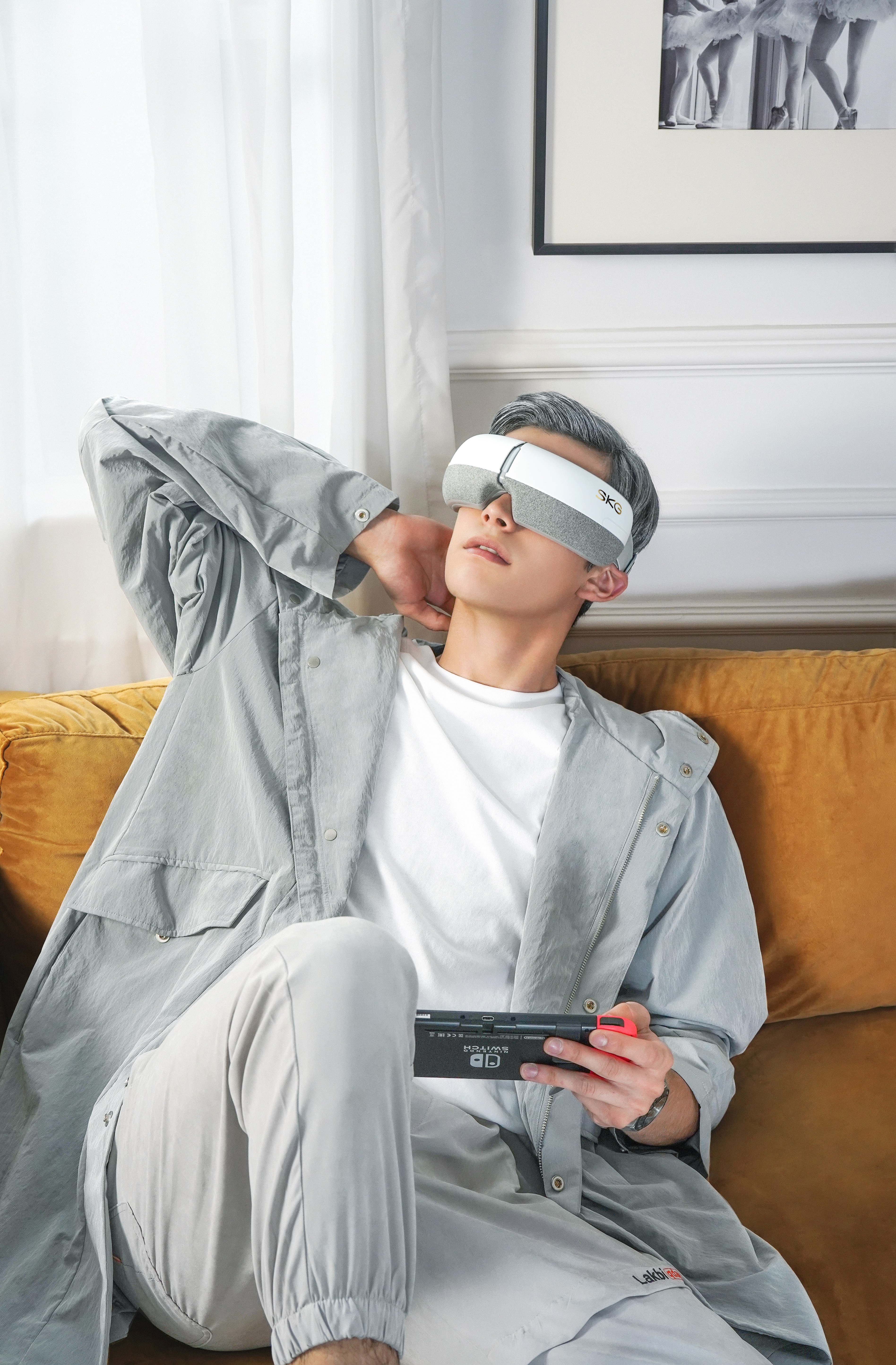 Mann mit Augenmaske, hält Gamecontroller, sitzt auf einem Sofa.