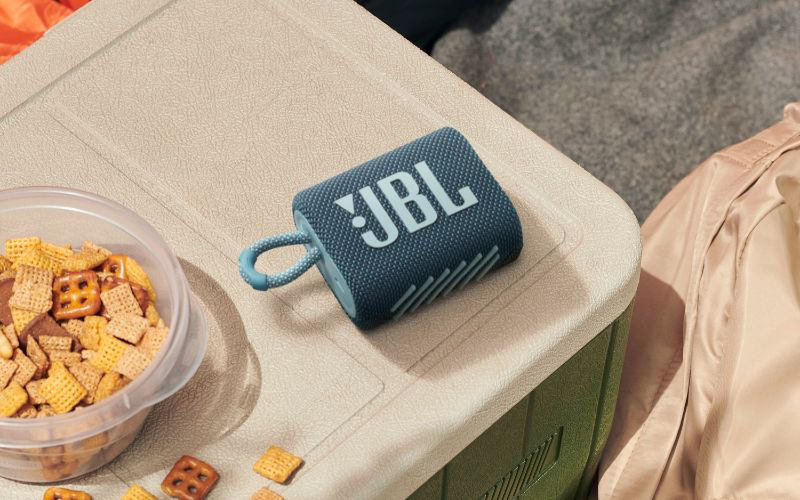 Mavi bir JBL hoparlör, atıştırmalıkların yanında bir soğutucu üzerine yerleştirilmiş.