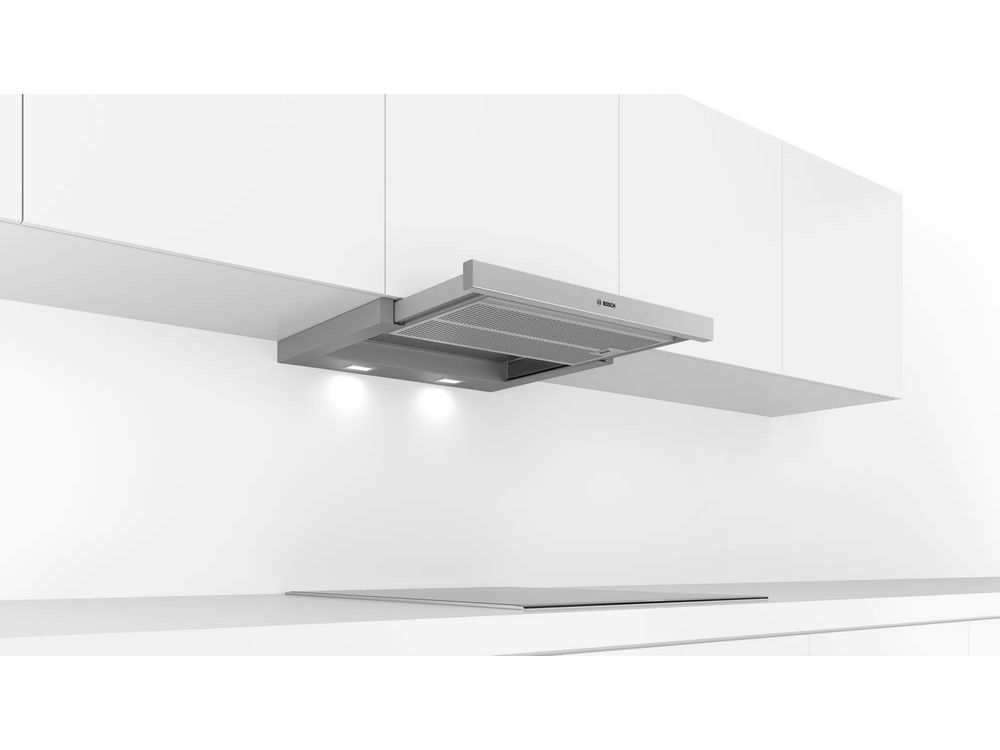 Una campana extractora de acero inoxidable con luces y filtro de malla plateada está montada en una pared blanca.