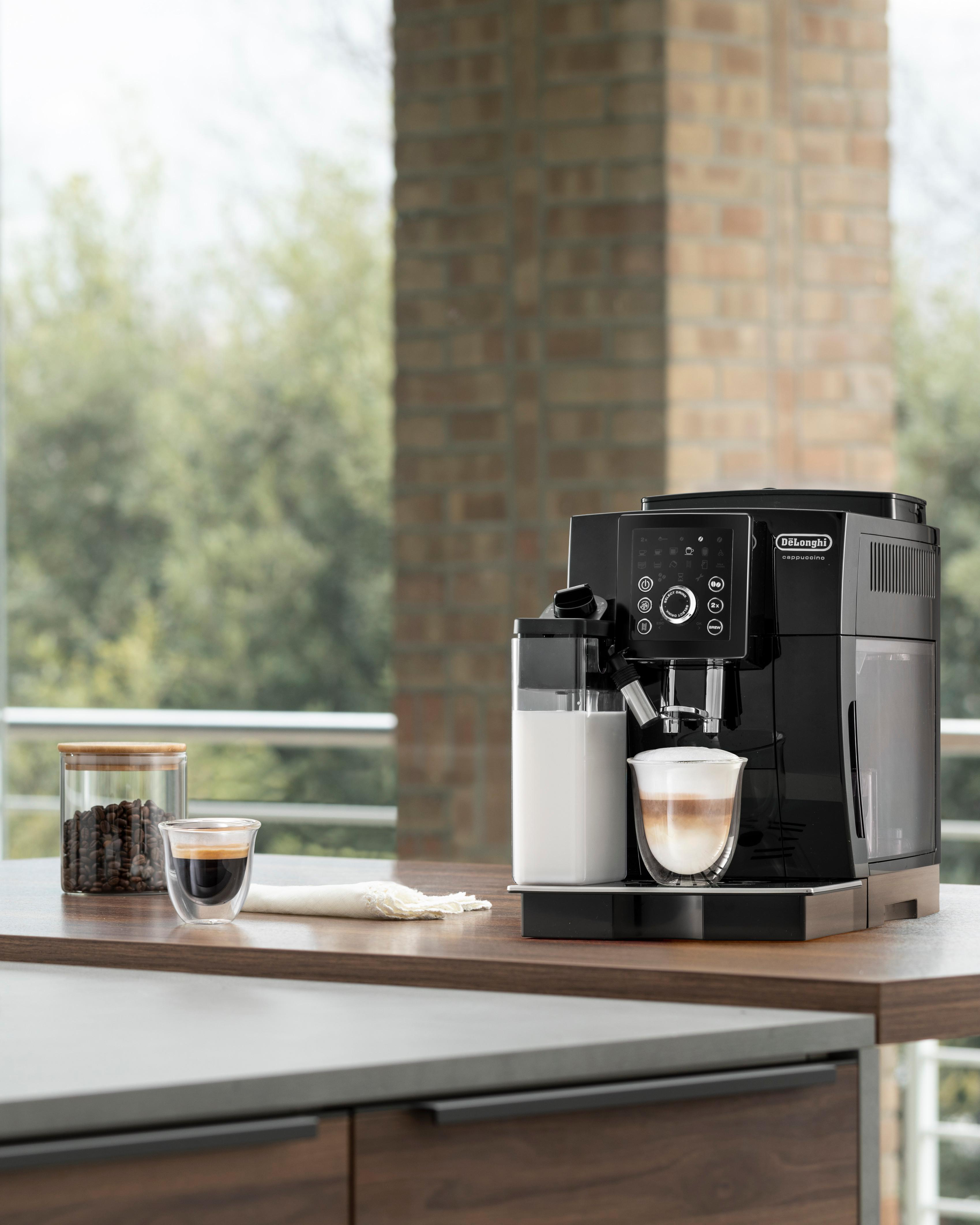 Schwarze und silberne Kaffeemaschine. Ein Glas Latte steht unter dem Auslauf auf einer Holzoberfläche.