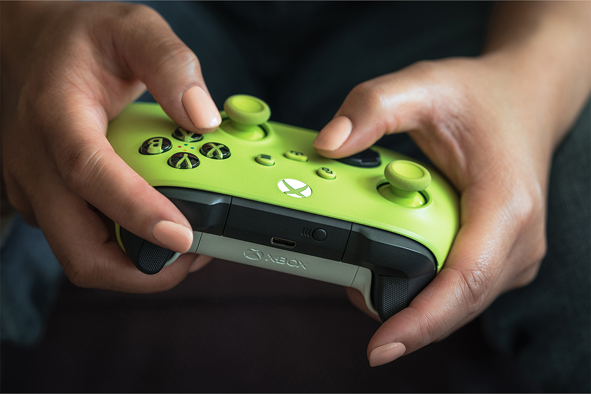 Hands holding a green Xbox controller, pressing buttons.