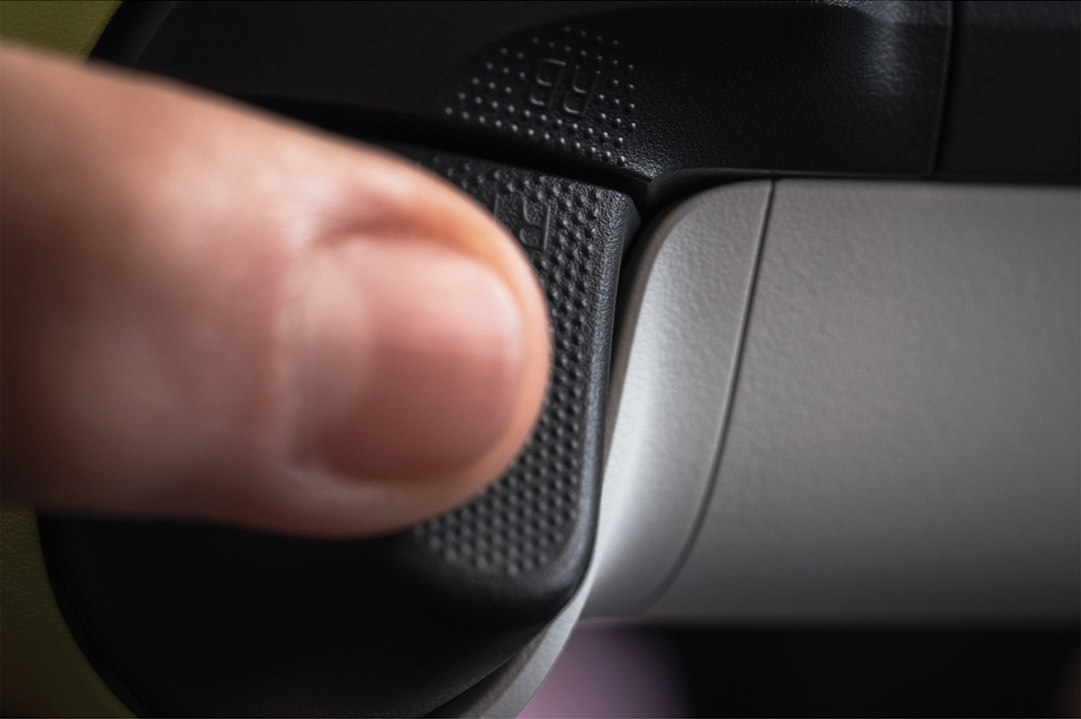 A finger presses the black button on a white and black game controller. Close up shot.