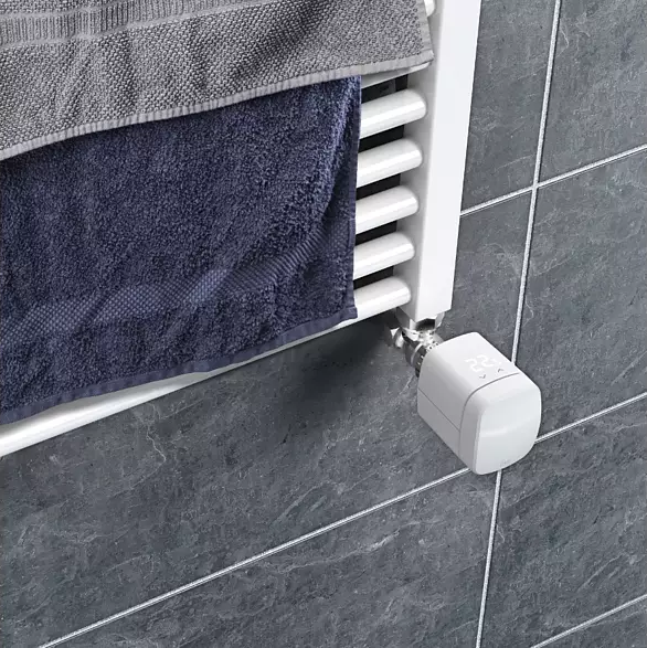 Ein weißer Heizkörper mit zwei Handtüchern und einem Thermostat. Die Wand ist gefliest.
