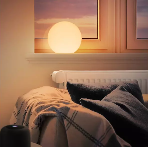 Ein leuchtendes kugelförmiges Licht sitzt auf einem Fensterbrett und beleuchtet einen Raum mit Kissen und einer Decke.