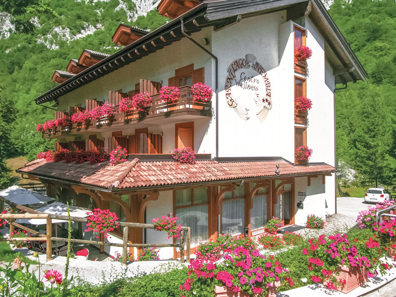 Un edificio bianco di un hotel con fiori rossi in vaso sui balconi. Una catena montuosa sullo sfondo.