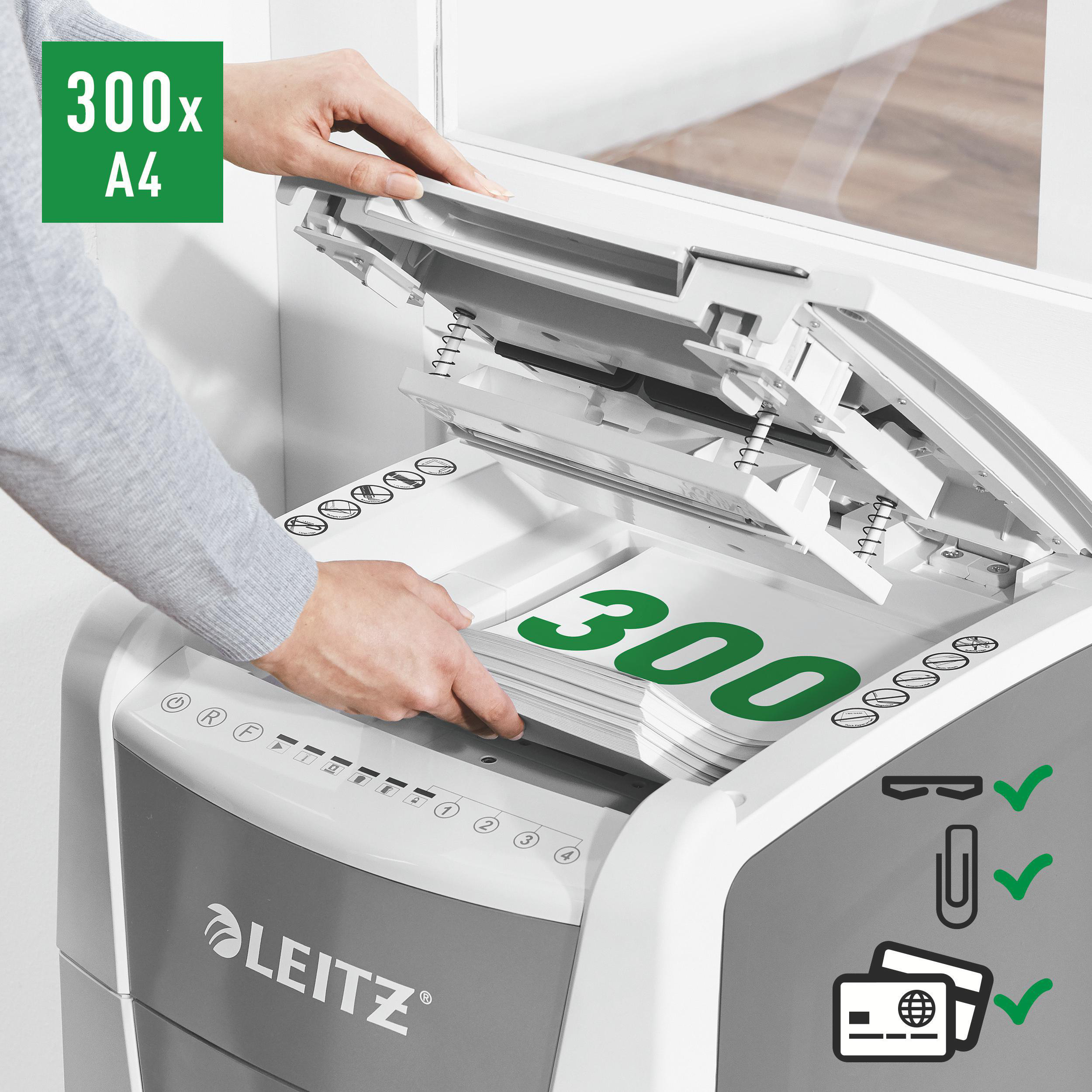 Eine Person führt Papier in einen Aktenvernichter ein. Der Schredder ist weiß und grau, mit Leitz gekennzeichnet.