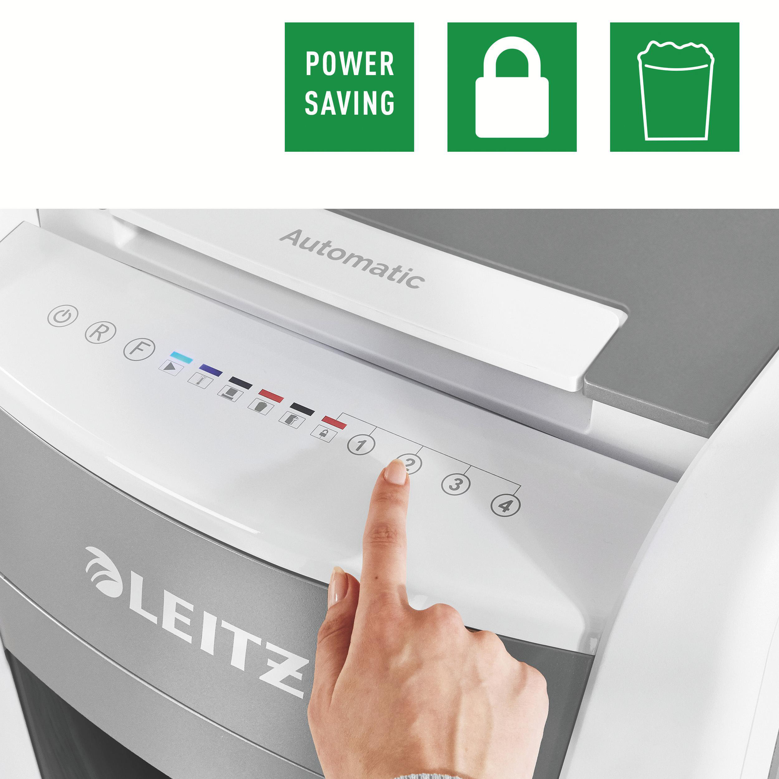 Eine Hand drückt eine Taste an einem Aktenvernichter. Grüne Symbole für Energiesparen, Schloss und Müll sind sichtbar.