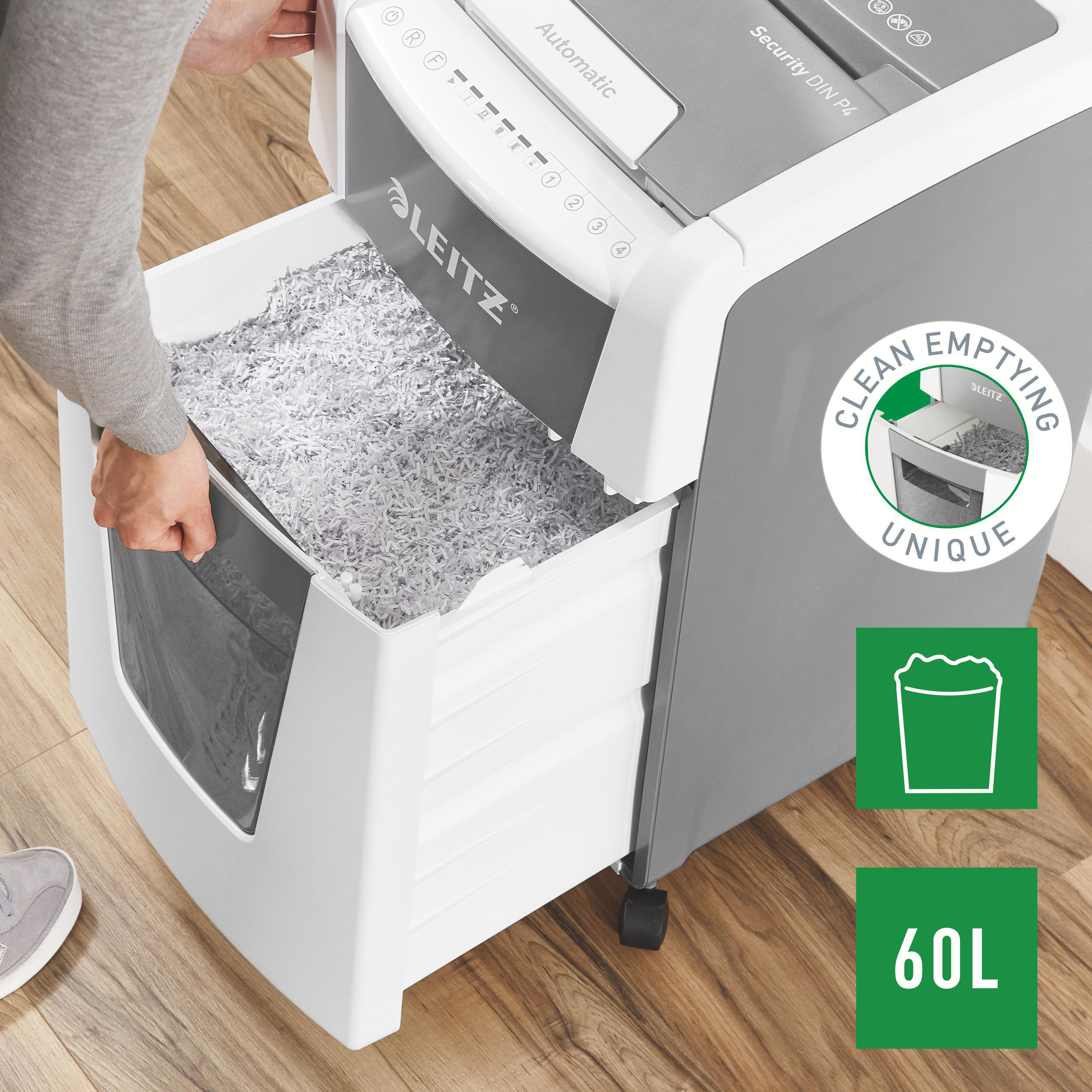 Eine Person leert einen Aktenvernichter. Gehäckseltes Papier füllt den Behälter. Die Maschine ist grau und weiß.