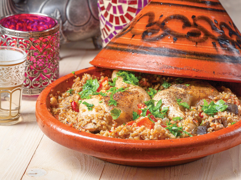 Piatto tagine marocchino con pollo, verdure e couscous, servito in una pentola di terracotta.