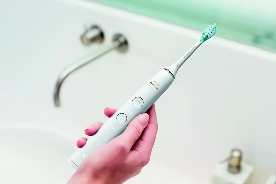 Electric toothbrush in hand, white. Bathroom background.