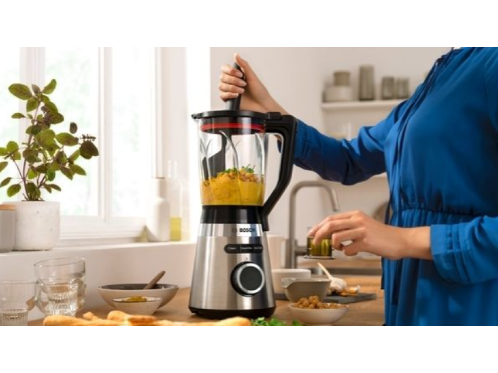 Una persona haciendo un batido con una licuadora en una encimera de cocina, con ingredientes.