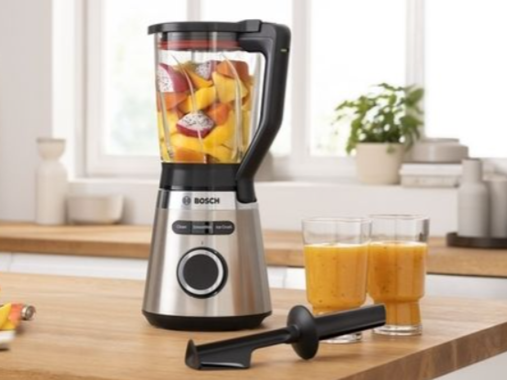 Licuadora con frutas, dos vasos de batido y una cuchilla negra sobre encimera de madera.