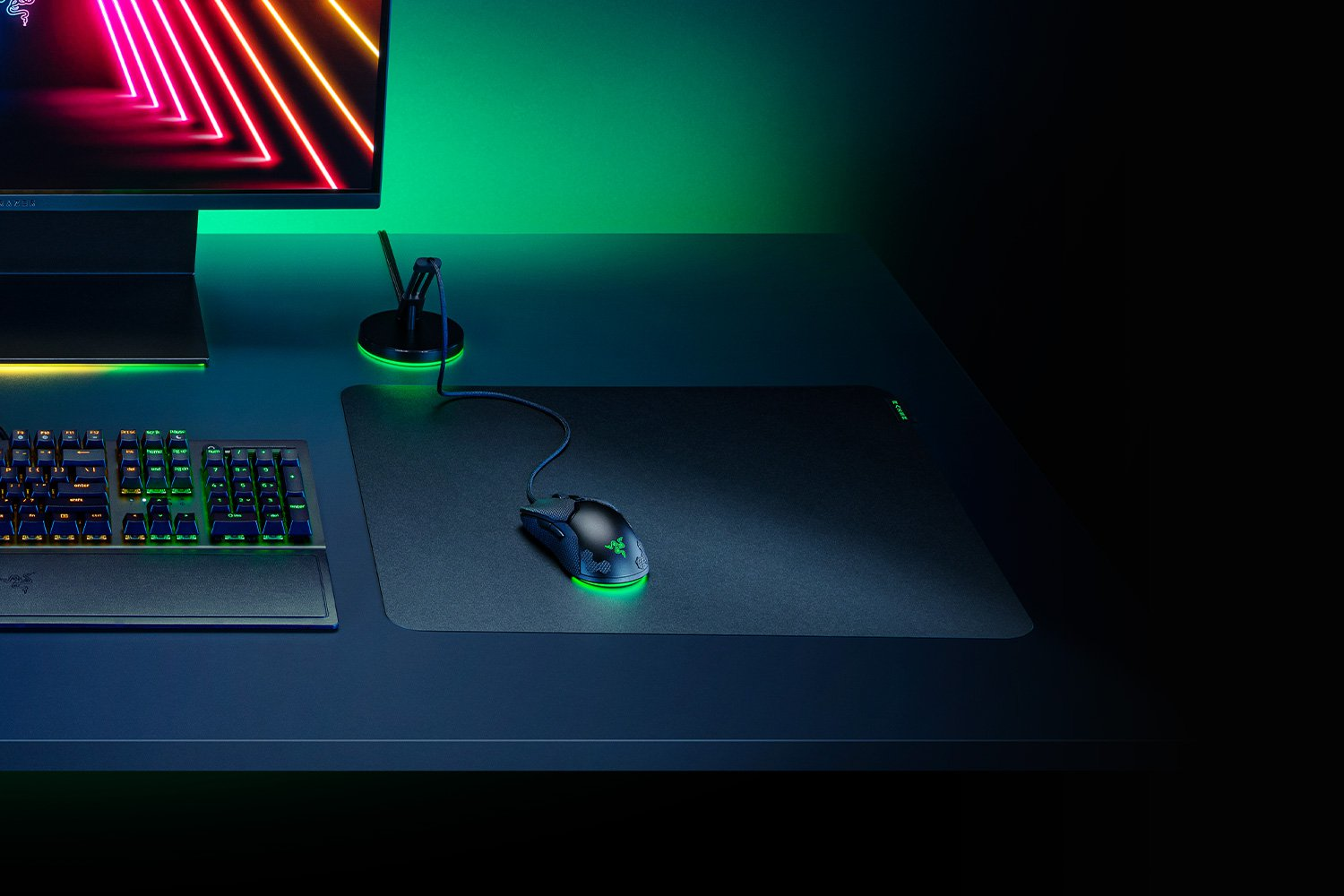 Dunkles Schreibtisch-Setup mit Razer-Tastatur, Maus und Mauspad. Neon-grüne Beleuchtung sichtbar.
