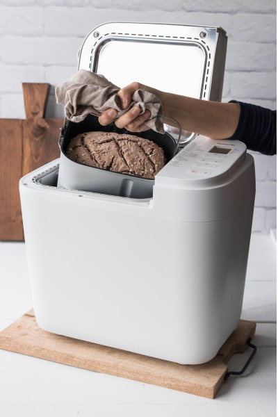 Egy személy kenyeret vesz ki egy fehér kenyérsütőből egy fa deszkán.