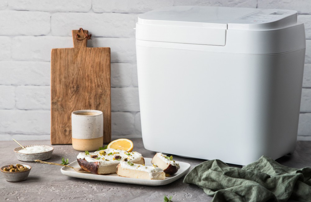 Kenyérsütő gép süteményekkel, kenyérrel és hozzávalókkal a pulton.