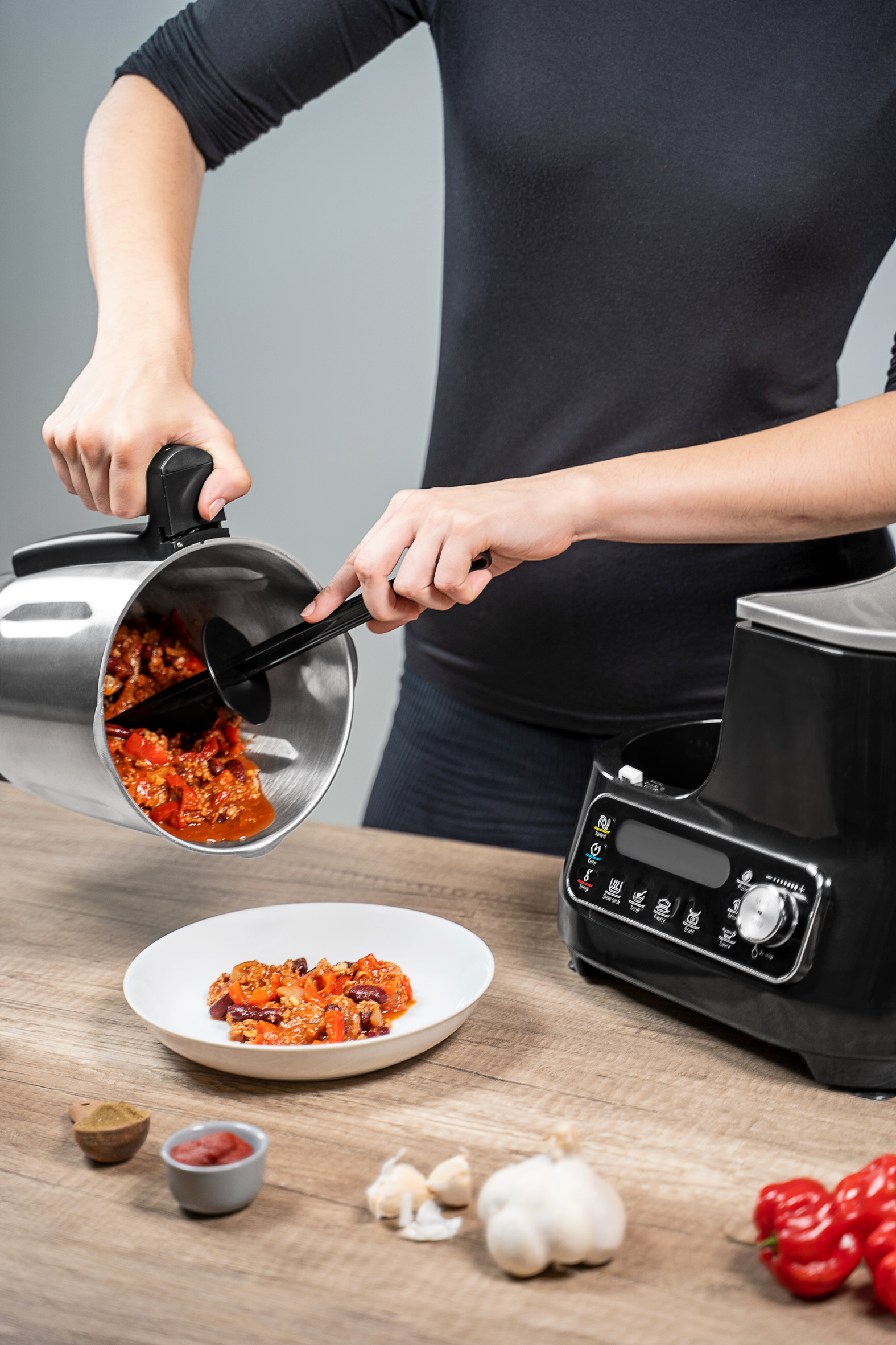 Une personne verse du ragoût d'une casserole argentée dans un bol blanc, près d'un robot culinaire.