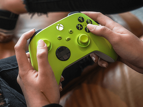 Eller parlak yeşil bir Xbox kontrolcüsü tutuyor. Düğmeler ve joystick'ler görünür.