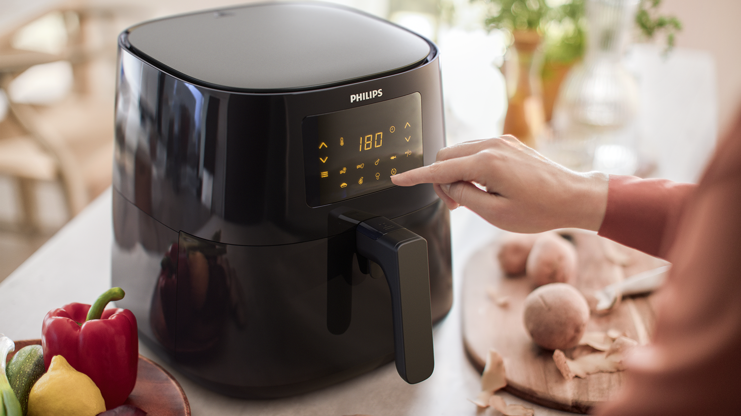 Zwarte airfryer met een hand die een knop indrukt.