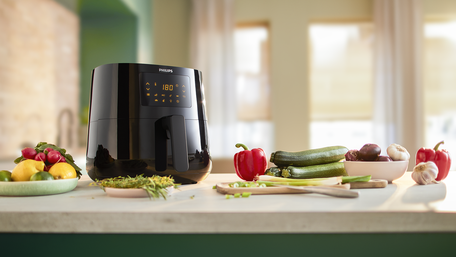 Zwarte Philips airfryer met groenten en kruiden op een aanrecht. Achtergrond is een keuken.
