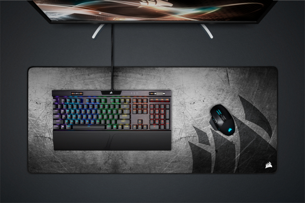Keyboard, mouse, and mousepad on a dark surface. Keyboard has rainbow lighting.
