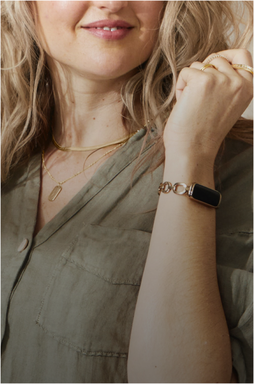 Bras de femme portant un bracelet doré et une montre intelligente, avec des bijoux en or.