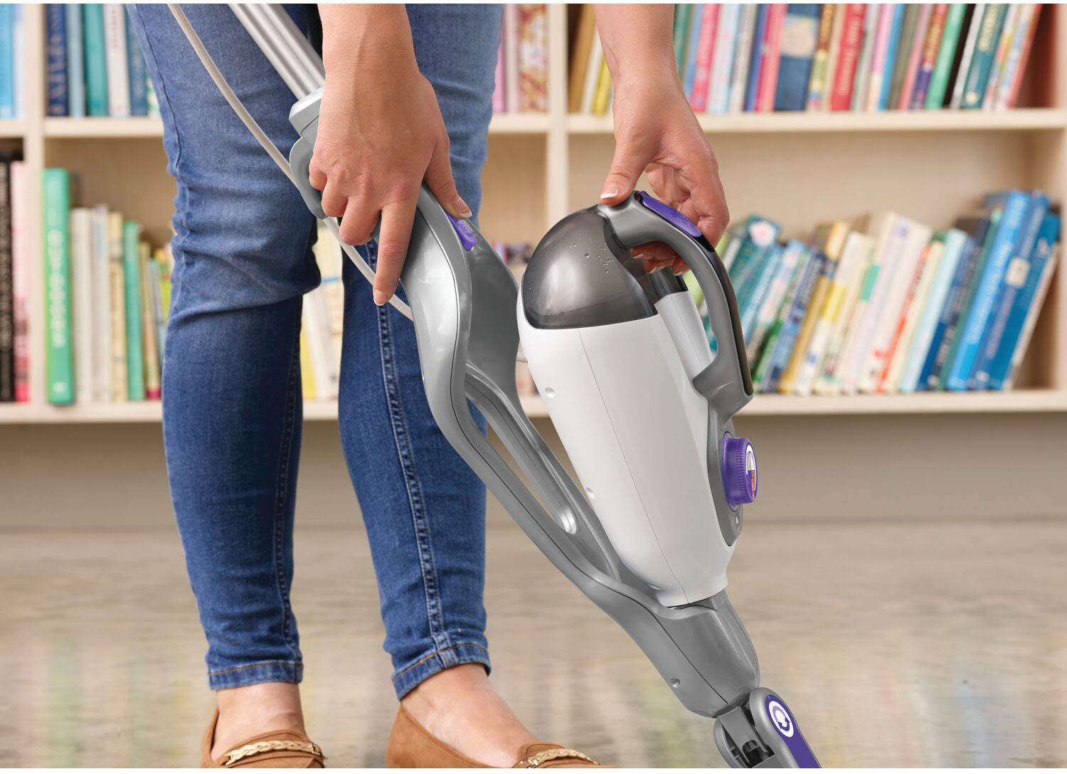 A person holding a steam mop. The background is a bookshelf with books.