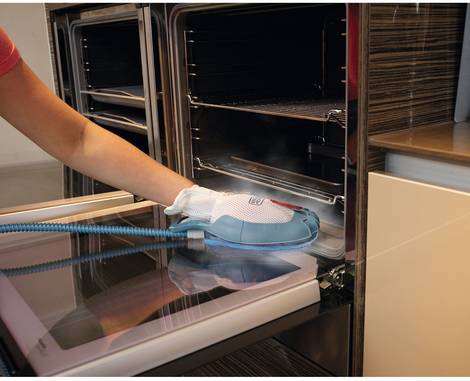 A hand uses a cleaning tool inside an oven. Tool is blue and white.