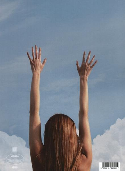 Eine Frau mit ausgestreckten Armen vor blauem Himmel mit Wolken.