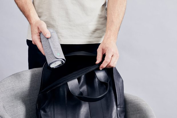 Une personne place un tensiomètre gris enroulé dans un sac en cuir noir. La personne porte une chemise blanche.