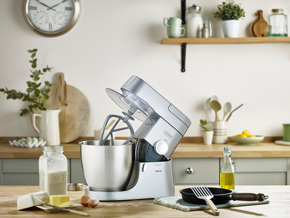 Een keuken met een keukenmachine, ingrediënten en een klok aan de muur.