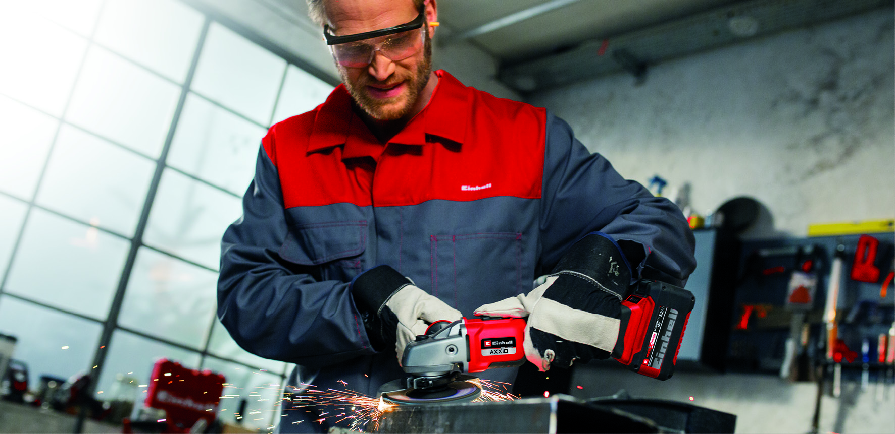 Ein Handwerker mit Schutzbrille nutzt eine rote Akku-Winkelschleifmaschine, die Funken wirft.