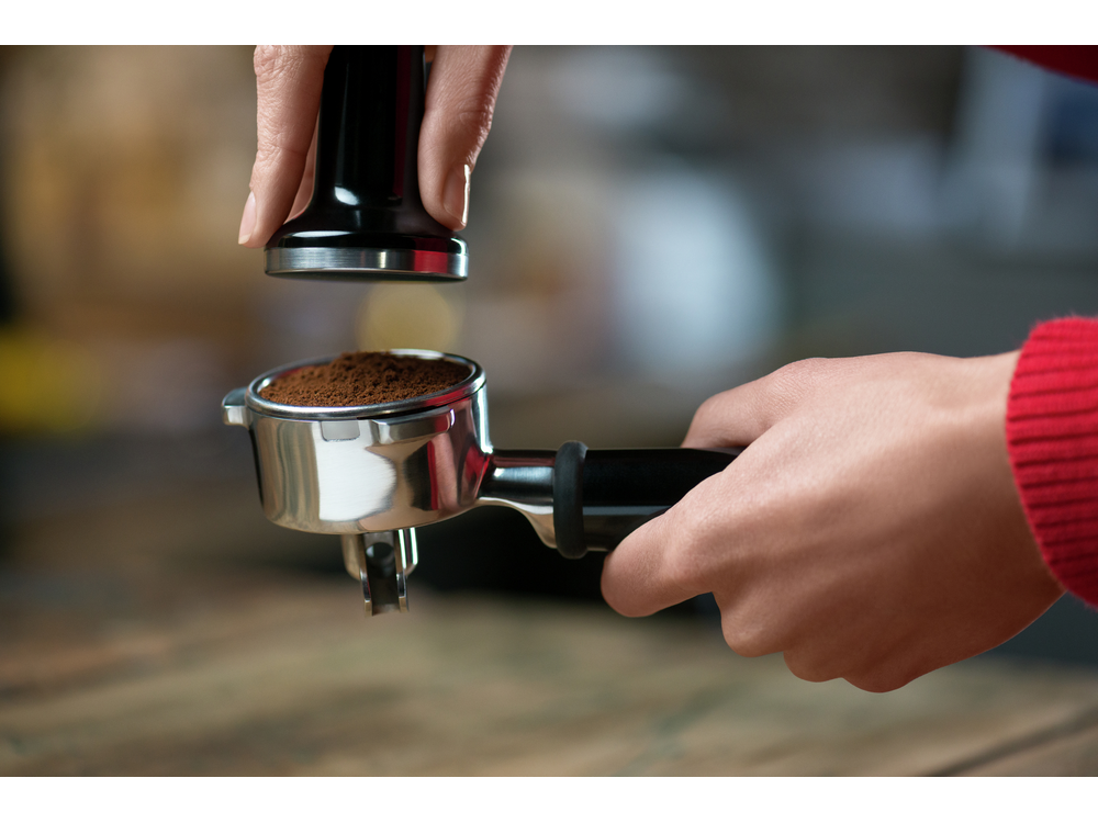 Manos sosteniendo un portafiltro con café molido y un tamper. Preparando café.
