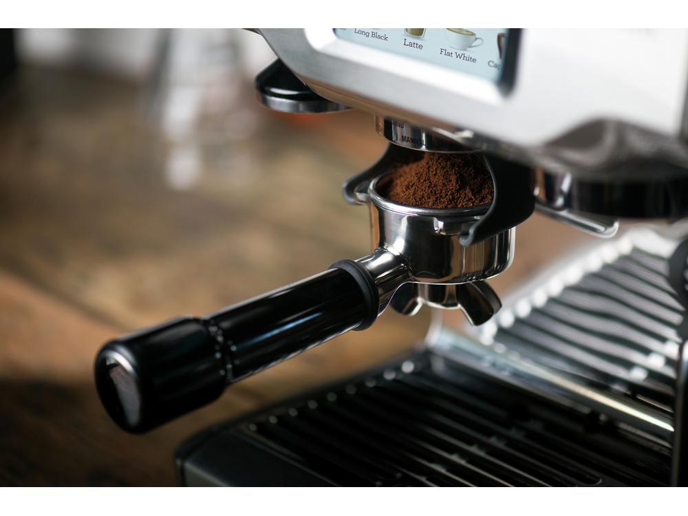 Una máquina de espresso plateada con café molido en el portafiltro.