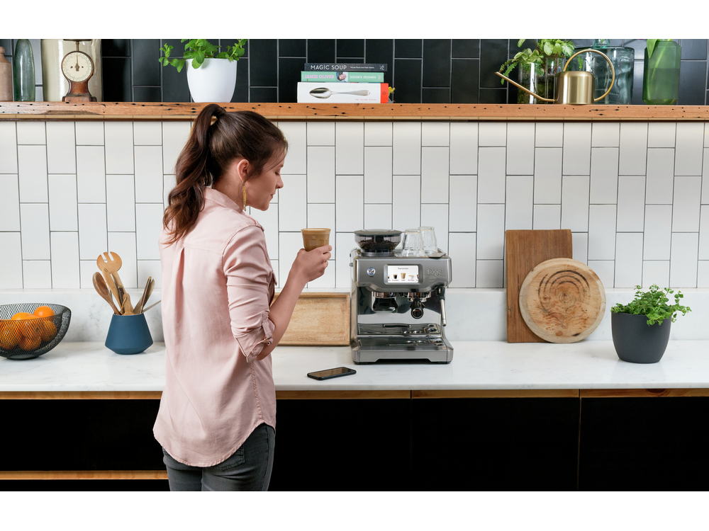 Una mujer sosteniendo una taza de café cerca de una cafetera.