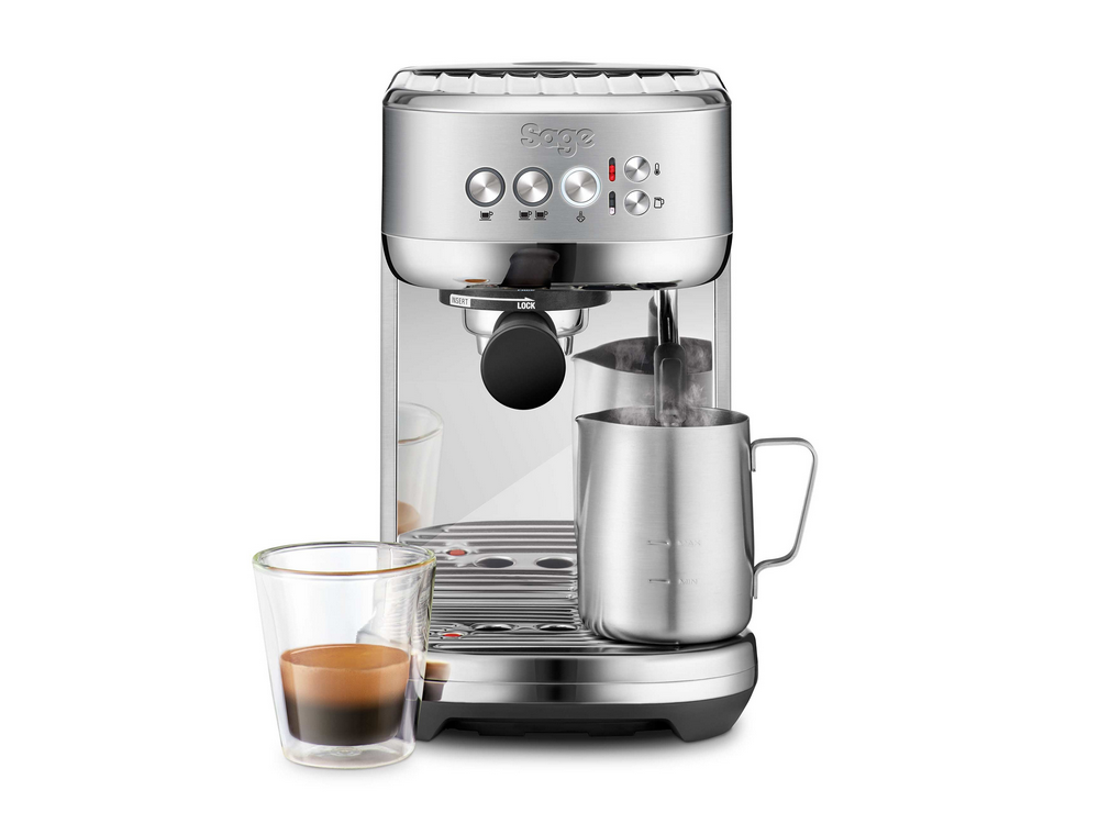 Máquina de espresso plateada con un vaso de espresso y una jarra de leche.