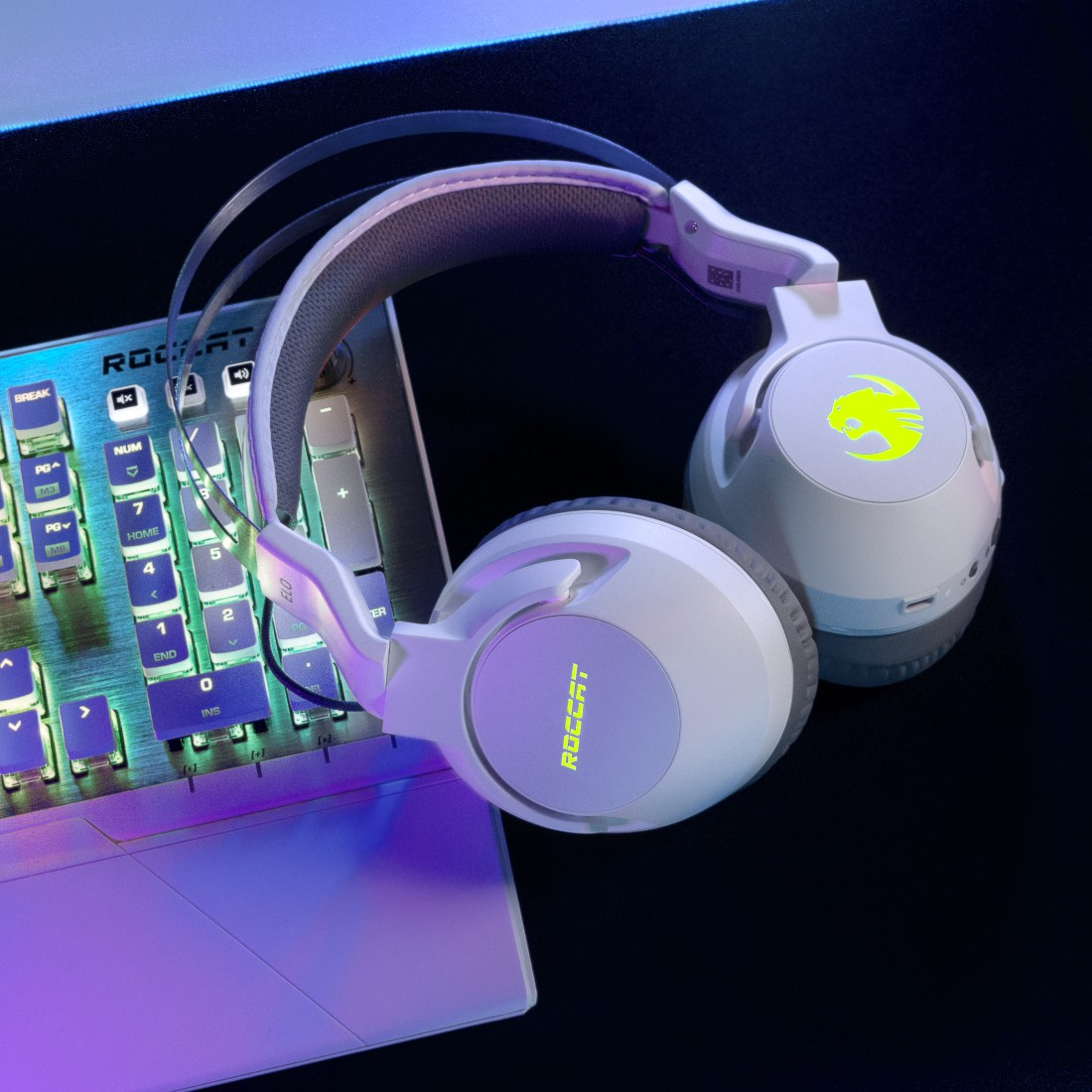 Weißes Roccat-Gaming-Headset auf einer Tastatur. Das Headset ist mit grünen Logos beleuchtet. Die Tastatur hat beleuchtete Tasten.