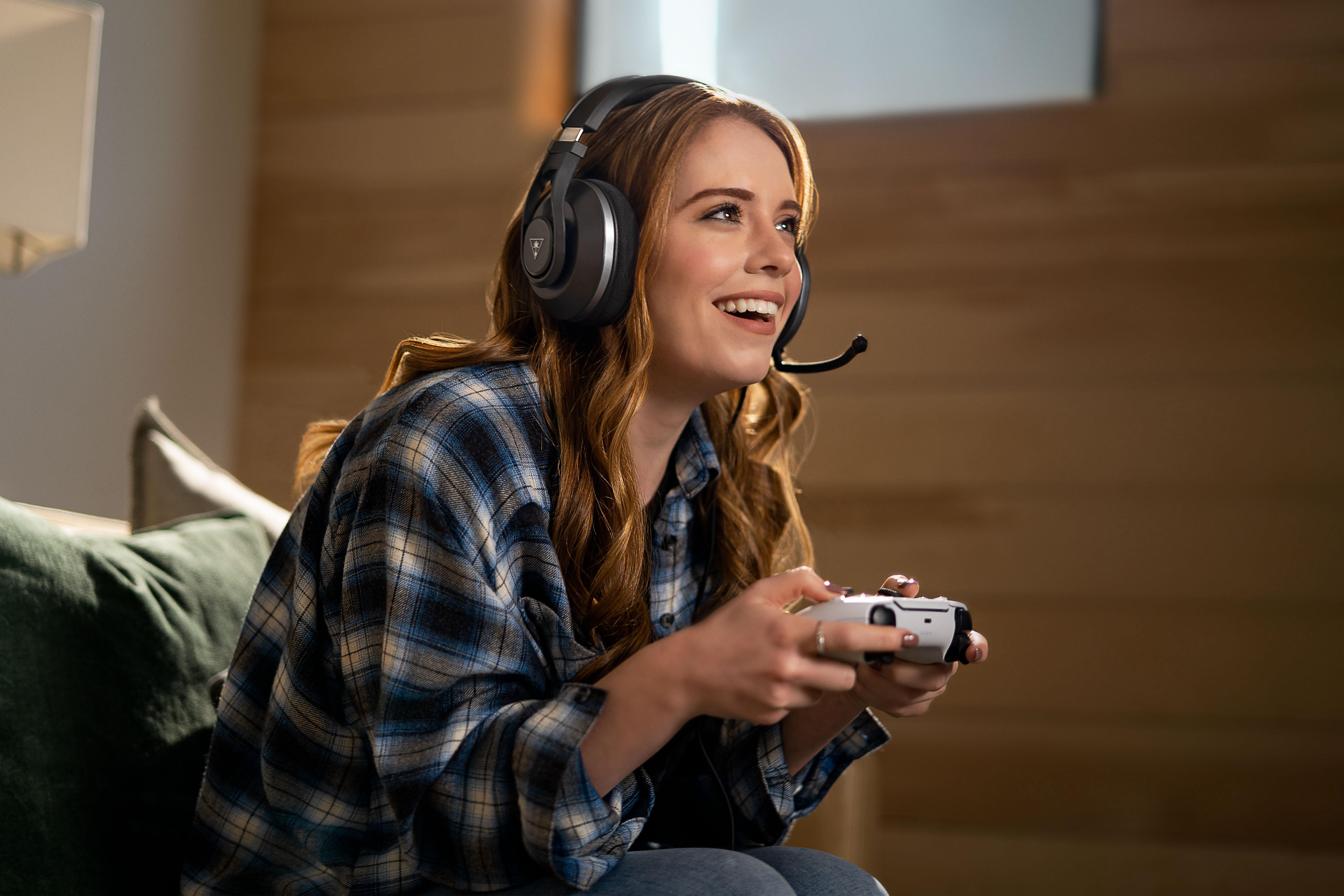 Frau spielt mit Headset und Controller. Lächelnd, zur Seite schauend, mit Fenster und Holzwand im Hintergrund.
