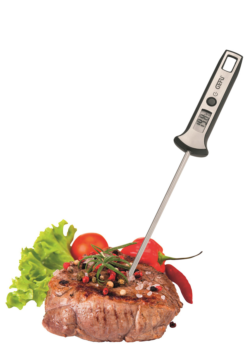 Ein Fleischthermometer in einem Steak, umgeben von frischen Kräutern und Gemüse.
